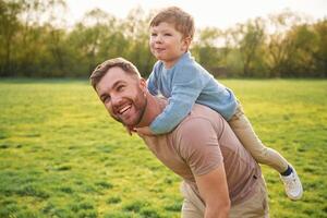 Sitting, on man's shoulders. Happy father with son are having fun on the field at summertime photo
