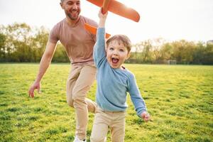 Orange, colored toy plane, playing. Happy father with son are having fun on the field at summertime photo