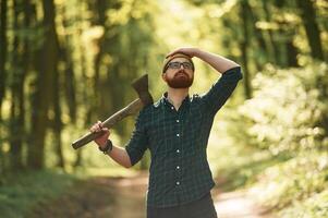 Looks up, holding an axe,. Bearded man is in the forest at daytime photo