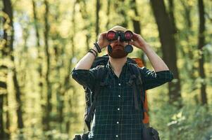 Discovering new place ,with ,binoculars. Bearded man is in the forest at daytime photo