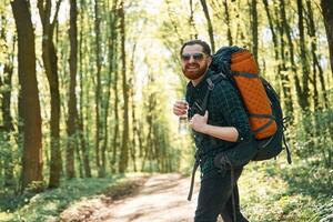 In ,glasses, and, with backpack. Bearded man is in the forest at daytime photo