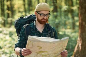 Old fashioned,, paper map in hands. Bearded man is in the forest at daytime photo