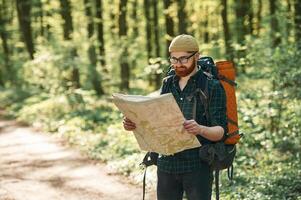 Old ,,fashioned paper map in hands. Bearded man is in the forest at daytime photo