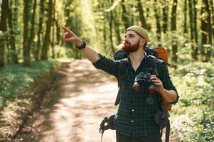 Discovering, new,, place with binoculars. Bearded man is in the forest at daytime photo