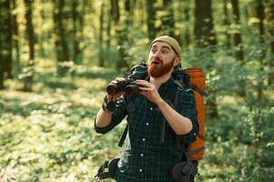 Discovering new place, with, binoculars. Bearded man is in the forest at daytime photo