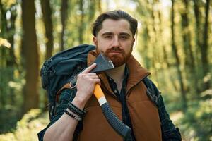 Shaving by using an axe. Bearded man is in the forest at daytime photo