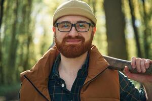 Holding an axe. Bearded ,man, is in the forest at daytime photo
