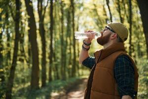 Drinking a water. Bearded man is in the, forest at daytime photo