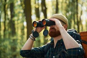 Tourist with binoculars. Bearded man is i,,n the forest at daytime photo