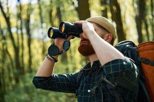 Using binoculars. Bearded,, man ,is in the forest at daytime photo