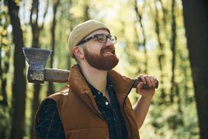 Holding, an axe. Bearded, man is in the forest at daytime photo