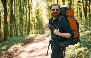 In glasses and with backpack. Bearded ,man is in the forest at daytime photo