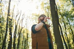Drinking ,a ,water. Bearded man is in the forest at daytime photo