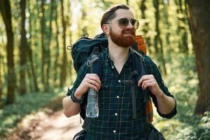With backpack. Bearded man is in the forest ,at daytime photo