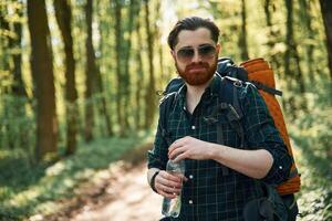 With,, backpack. Bearded man is in the forest at daytime photo