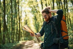 Using ,the ,map. Bearded man is in the forest at daytime photo
