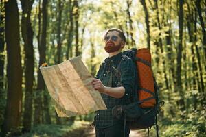Old fashioned paper map in hands. Bearded ,man is in the forest at daytime photo