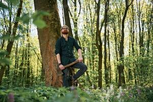 Holding an, axe. Bearded ,man is in the forest at daytime photo