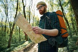Reading the map, looking for a way. Bearded man is in the forest at daytime photo