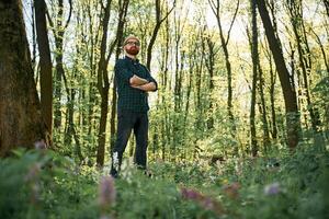 With arms crossed. Bearded man is in the forest at daytime photo
