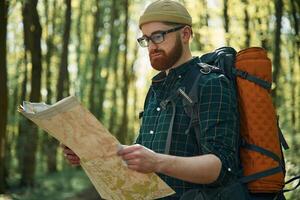 Reading, the map, looking ,for a way. Bearded man is in the forest at daytime photo