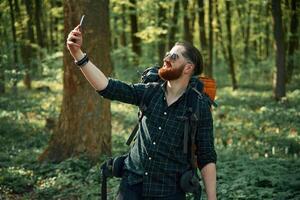 Phone in hand... Bearded man is in the forest at daytime photo