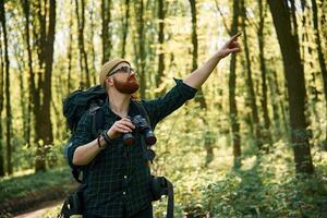 Tourist, with binoculars. Bearded man is in the forest at daytime photo