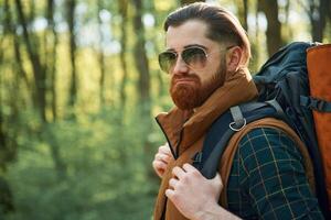 In ,cool ,sunglasses. Bearded man is in the forest at daytime photo