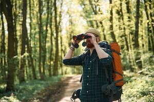 Tourist with binoculars.. Bearded, man is in the forest at daytime photo