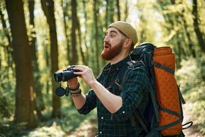 Using binoculars. Bearded man, is, in the forest at daytime photo