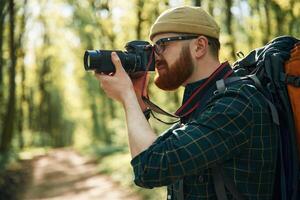 Photographer, with camera. Bearded, man is in the forest at daytime photo