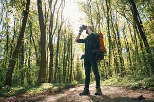 Looking far away by using binoculars. Bearded man is in the forest at daytime photo