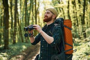 Using binoculars.. Bearded man is in the forest at daytime photo