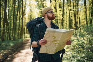 Reading the map,, looking for a way. Bearded man is in the forest at daytime photo