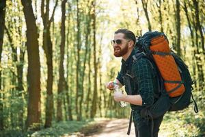 In glasses and with backpack.. Bearded man is in the forest at daytime photo