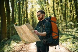 Old fashioned ,pape,r map in hands. Bearded man is in the forest at daytime photo