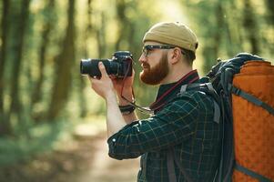Professional photographer. Bearded man is in the forest at daytime photo