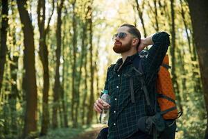 With backpack. Bearded man is in,, the forest at daytime photo