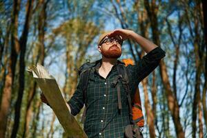 Big, paper map. Bearded man is in the forest at daytime photo