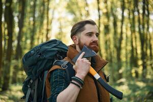 Shaving by ,using an axe. Bearded man is in the forest at daytime photo