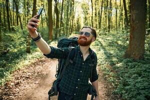 Phone in, hand. Bearded man is in the forest at daytime photo