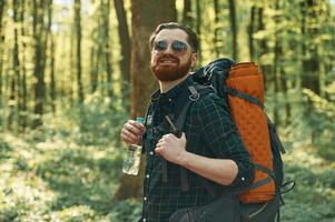 Bottle,, of water, holding. Bearded man is in the forest at daytime photo