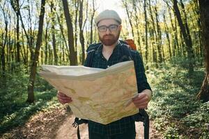 Reading ,the map, looking for a way. Bearded man is in the forest at daytime photo