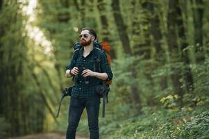 On the ,pathway with binoculars. Bearded man is in the forest at daytime photo