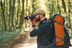 Photographer, with camera. Bearded man is in the forest at daytime photo