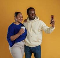 Making selfie. Happy black couple are together against yellow background photo