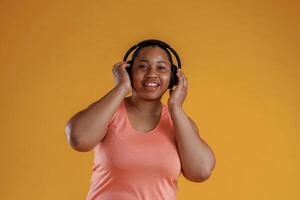 Front view, in headphones,,, listening to music. African American woman is in the studio against yellow background photo