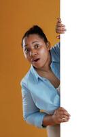 White, copy,, space wall, hiding behind it. African American woman is in the studio against yellow background photo