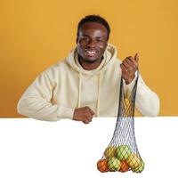 Smiling, holding bunch of fruits against white copy space. Black guy is on yellow background photo