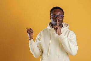 Keep ,the secret, showing behind by the finger. Black guy is against yellow background photo